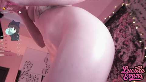 Media: Video of a pale-skinned, nude woman, seen from behind, in a dimly lit bedroom with pink lighting. The background features a wall with a star pattern and a chat window showing a user named \"LucilleGowns.\