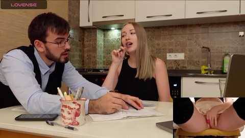 Media: Video of a man and woman in a modern kitchen. He's dressed in a white shirt and black vest, she's in a black dress, holding a sandwich.