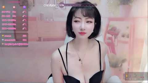 Media: A video of an Asian woman with fair skin and short black hair, wearing a black bra, sitting indoors with a soft pink background and streaming overlays.