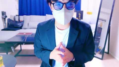 Media: Video of an Asian man in a dark suit and blue-tinted glasses, wearing a face mask, standing in a modern living room with a pool table, white sofa, and blue curtains.