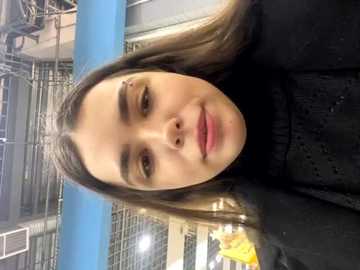 Media: Video of a young woman with fair skin, long blonde hair, and a black turtleneck sweater, taken indoors near a blue railing and metal structures.