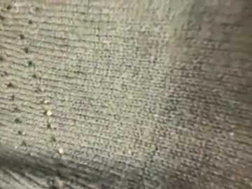 Media: A close-up video of a textured, beige fabric with a woven pattern, featuring small, evenly spaced stitches and a subtle sheen. The image is slightly blurred, focusing on the fabric's intricate detail.