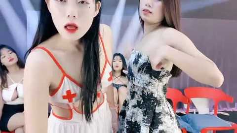 Media: Video of four Asian women in provocative, semi-transparent nurse costumes with red crosses, posing suggestively. Background includes modern, minimalistic decor with red chairs.