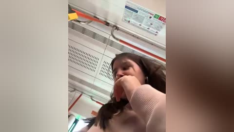 Media: A video of a young woman with long brown hair eating a peach inside a bus. She wears a pink sweater. The background includes bus ceiling panels and a yellow emergency exit sign.