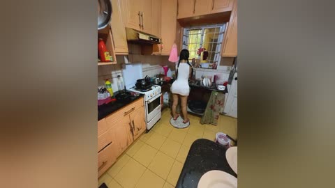 Media: A video of a small kitchen with light wood cabinets, a woman in a white dress standing on a kitchen scale, and a cluttered countertop.