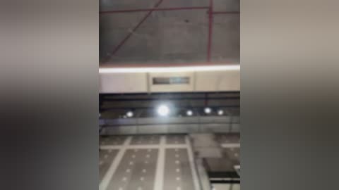 Media: A video shows a dimly lit, empty, modern airport terminal with a large, bright ceiling light, red electrical lines, and white and gray tiled flooring. The image is slightly blurred.