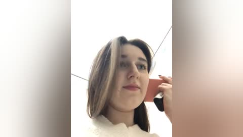 Media: A video of a young woman with straight brown hair, light skin, and a white bathrobe, taking a selfie in a dimly lit bathroom. The image is slightly blurry.