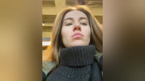 Media: Video of a young woman with fair skin, straight brown hair, and full lips, wearing a dark grey turtleneck sweater, in a dimly lit, industrial background with exposed beams.