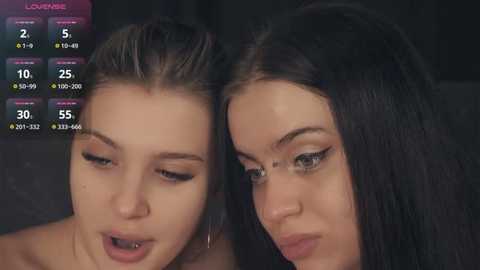 Media: Video of two young women with fair skin and dark hair, looking at a screen displaying their live stream statistics. They have makeup and are sitting closely together.