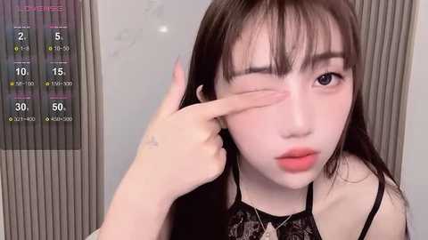 Media: A video of a young Asian woman with long dark hair, fair skin, and pink lipstick, wearing a black lace top. She is adjusting her makeup in front of a mirror with a digital clock showing 5:10.