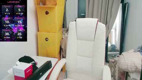 Media: Video of a cluttered bedroom with a white gaming chair, yellow storage boxes, a bed with a beige blanket, and a small TV showing a game screen.