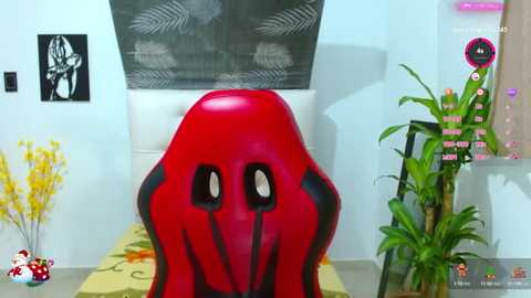 Media: Video of a red, octopus-shaped chair with black accents, set against a wall with a fern painting, potted plants, and yellow flowers.