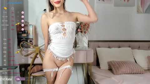 Media: Video of a slender, fair-skinned Asian woman in a white, lace-up corset and matching garter belt, standing in a pink-lit bedroom with floral arrangements and a plush bed.