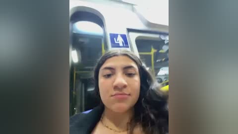 Media: Video of a young Latina woman with long, dark hair, wearing a black jacket, seated in a public bus. A blue and yellow sign with a white wheelchair symbol is visible above her head.