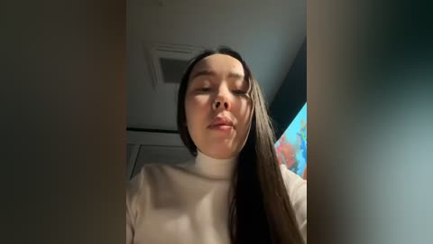 Media: A video of a young Asian woman with long brown hair, wearing a white turtleneck, looking slightly to the right with a neutral expression.