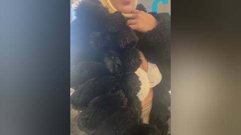 Media: Video of a woman in a black fur coat, partially unzipped to reveal a white lace bra and fishnet stockings. Her face is partially obscured. Background is a blurred, neutral-toned room.