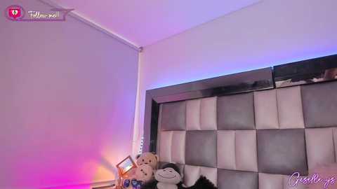 Media: Video of a modern bedroom with a gray and white tufted headboard, plush teddy bear, and colorful LED lights.