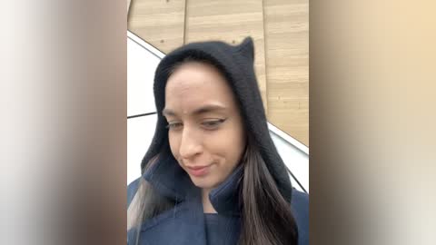 Media: A video of a young woman with long, straight hair, wearing a black cat ear hat, smiling. She has fair skin and is standing against a wooden wall.