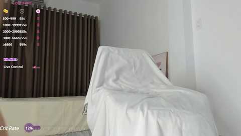 Media: A video of a white recliner chair covered with a white sheet, situated in a minimalist, well-lit room with beige walls and brown curtains.