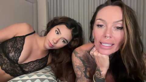 Media: Video of two women; one with long dark hair, wearing a black lace bra, and another with long hair, tattoos, and a nose ring, smiling.