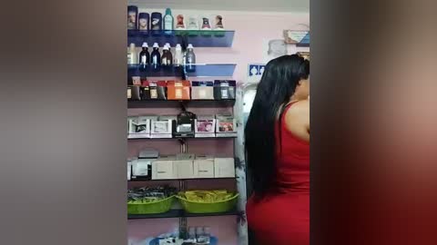 Media: A video of a woman with long black hair in a tight red dress, facing a shelf stocked with beauty products and baskets.