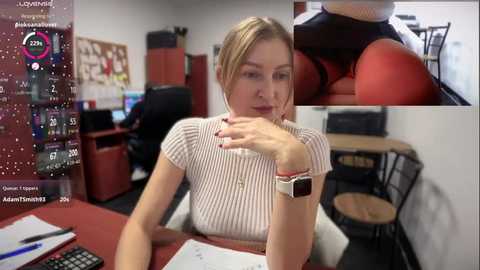 Media: Video of a blonde woman in a striped top, seated at a red desk, with a close-up of her red panties. Office background with a calendar and computer screen.