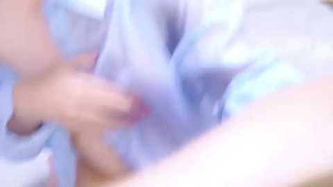 Media: A blurred video of a person in light blue clothing, possibly a shirt, with a hand touching the chest. The image has a soft focus, making it difficult to discern details.