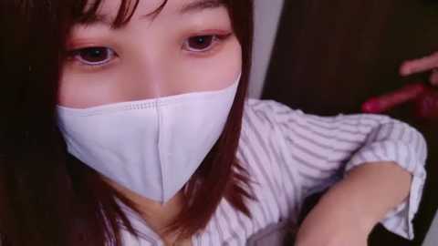 Media: A video of an Asian woman with straight, dark hair, wearing a white face mask and a striped shirt, taken from an overhead angle.