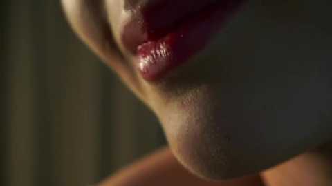 Media: A close-up video of a woman's lips, painted in glossy red lipstick, partially obscured by a hand. The background is blurred, featuring vertical wooden slats, possibly from a door.