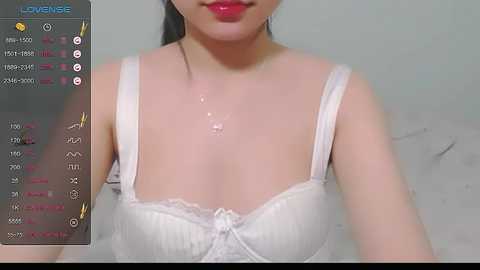 Media: Video of an Asian woman with fair skin, wearing a white lace bra, with semen dripping down her chest. Background is a plain, light-colored wall.