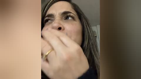 Media: A video shows a close-up of a woman with long, straight, dark hair, partially obscuring her face with her hand. She wears a gold ring on her right hand. The background is blurred.