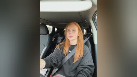 Media: Video of a young woman with long, straight, reddish-brown hair, wearing a black hoodie, driving in a car, with a safety belt across her chest.