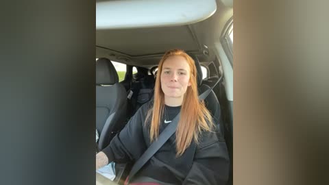 Media: A video of a young woman with long, straight red hair, wearing a black t-shirt and a seatbelt, sitting in a car's backseat.