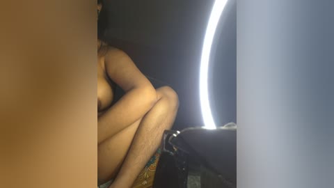 Media: A video shows a nude, light-skinned woman with medium-sized breasts sitting on a car seat. She covers her breasts with her arm. The background features a bright, circular light.