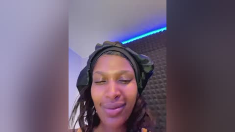 Media: A video of a smiling, light-skinned Black woman with long braids wearing headphones and a headband, set against a dark brick wall with blue LED strip lighting.