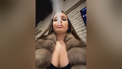 Media: A video of a woman with long hair, wearing a fur coat, large hoop earrings, and a plunging neckline, posing in a dimly lit room with exposed brick walls.