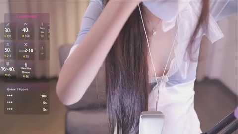 Media: A video of a woman with long, straight black hair, wearing a white top and beige pants, adjusting her white earbuds, set in a modern living room with light-colored walls and a sofa.