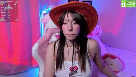 Media: Video of a young Asian woman with long black hair, wearing a red cowboy hat, white tank top, and necklace, sitting on a white gaming chair in a brightly lit room with red and blue lighting.