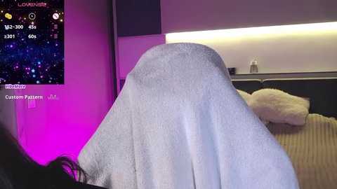 Media: A video of a person with a large, fluffy white blanket covering their head, in a dimly lit bedroom with a soft pink light. A digital overlay shows a starry sky and night mode.