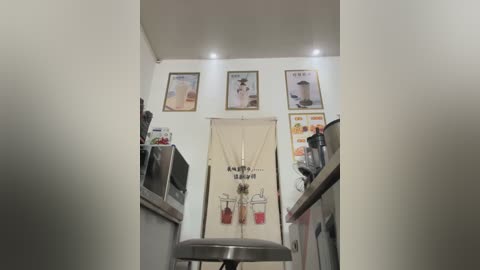 Media: Video of a minimalist, modern kitchen featuring a stainless steel counter, a white apron with cartoon characters, and three framed beverage posters on a white wall.