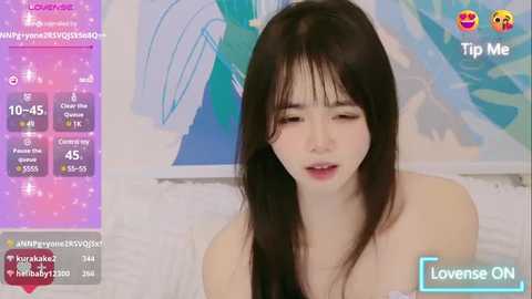 Media: Video of an East Asian woman with long, straight black hair, fair skin, and light makeup. She wears a strapless top. The background features abstract art and a \"Loveense ON\" watermark.