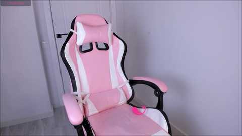 Media: A video of a pink gaming chair with white accents and adjustable armrests, set against a plain white wall and light grey floor.