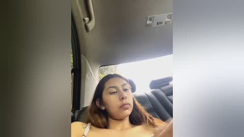 Media: Video of a young woman with medium skin tone, long brown hair, and closed eyes, lying on a car seat, taken from the front passenger seat.