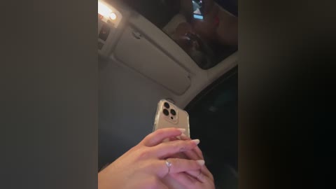 Media: A video captures a person taking a selfie in a dimly lit car, with visible reflections on the rearview mirror. The subject has light skin, manicured nails, and a ring on their finger.