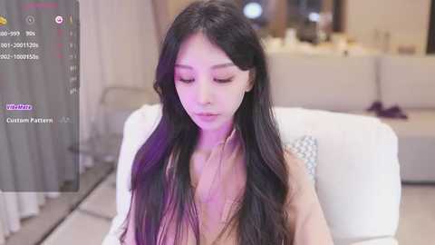 Media: A video of an Asian woman with long, straight black hair and pale skin, sitting in a modern living room. She wears a beige top.