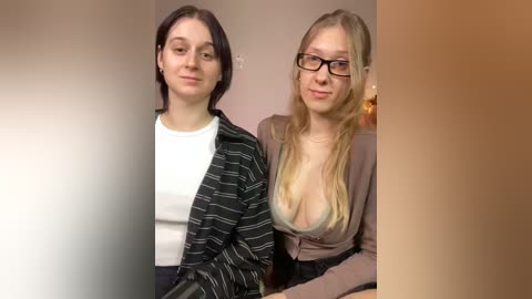 Media: A video of two young women with fair skin and light hair, one with short dark hair in a striped sweater, the other with long blonde hair in a low-cut top, standing close together.