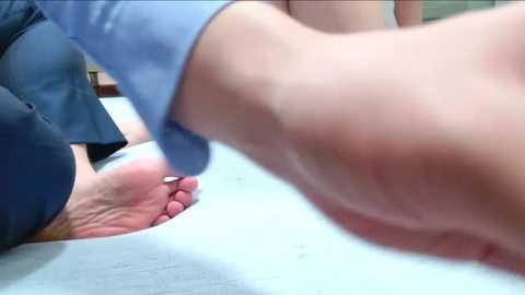 Media: A video shows a person in a blue suit bending over a seated individual, whose feet are being massaged. The background features a light-colored, textured surface.