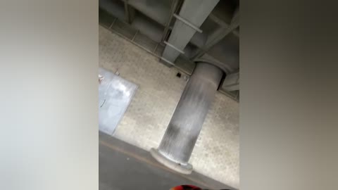 Media: A video of a metal support column and a white plastic pipe in an industrial setting. The floor is covered with a patterned tile. The image is taken from a low angle, emphasizing the vertical structures.