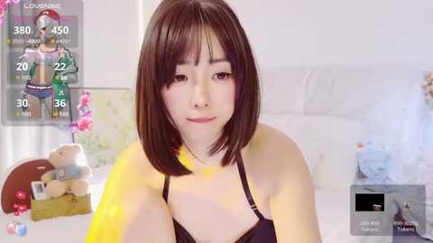 Media: A video of a young Asian woman with short black hair, fair skin, and a slender build, wearing a black bra, in a brightly lit bedroom.