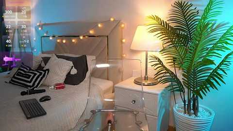 Media: Video of a modern bedroom with a white bed, black and white striped pillows, a glass desk, a potted plant, a white nightstand with a lamp, and fairy lights.